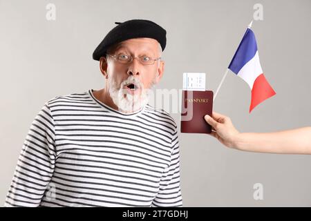 Schockierter Mann und Frau mit Flagge von Frankreich und Pass auf hellem Hintergrund Stockfoto