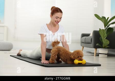 Glückliche junge Frau, die Yoga auf Matte mit ihrem süßen Hund zu Hause praktiziert Stockfoto