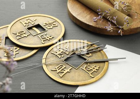 Akupunkturnadeln, Moxastöcke und antike chinesische Münzen auf grauem Holztisch, Nahaufnahme Stockfoto