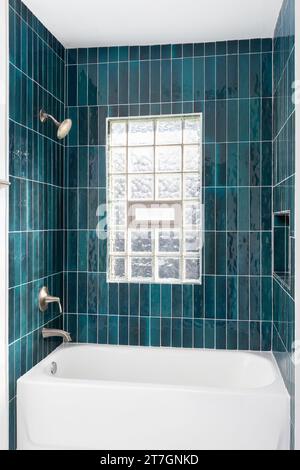 Das Badezimmer verfügt über eine Dusche mit leuchtend blauen vertikalen Glasfliesen, eine eingebaute Nische und ein Fenster mit Glasblöcken. Stockfoto