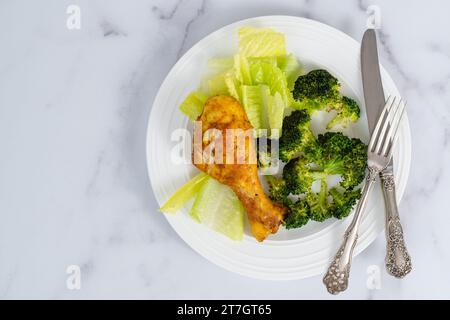 Ein Teller mit einem im Ofen gebackenen Hähnchenkegel und Brokkoli, serviert mit frischem Salat, Nahaufnahme auf einem Marmor-Küchentisch, Blick von oben mit einer Kopie sp Stockfoto