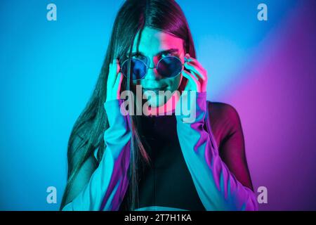 Futuristisches Studio-Porträt mit Neonlichtern von nicht binären Geschlechtern, die Sonnenbrillen tragen Stockfoto