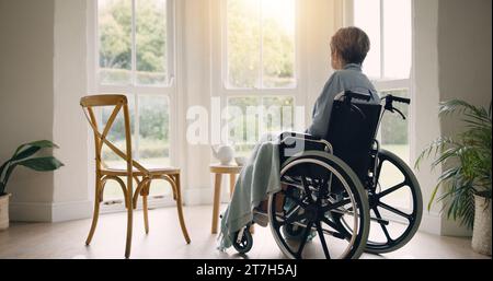 Rollstuhl, alte Frau oder denkend und einsam durch Fenster im Pflegeheim oder Ruhestand mit Depression. Nostalgie, trauriges Gedächtnis oder depressive ältere Menschen Stockfoto