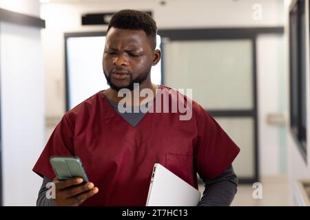 afroamerikanischer Arzt mit Smartphone im Krankenhauskorridor Stockfoto