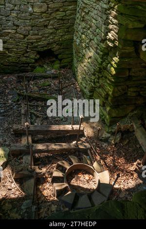 Ansicht einer schattigen steinernen Ruine mit Laub bedeckt, einem verrosteten Metallrahmen und einem radähnlichen Eisenteil in der Sonne, Robert H. Treman State Park, New York. Stockfoto