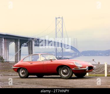 1964 Pressebild des roten Jaguar E-TYPE Serie 1 Coupé, TES 1, mit der neu eröffneten Forth Road Bridge im Hintergrund Stockfoto