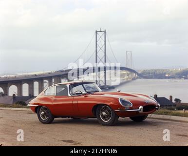 1964 Pressebild des roten Jaguar E-TYPE Serie 1 Coupé, TES 1, mit der neu eröffneten Forth Road Bridge im Hintergrund Stockfoto