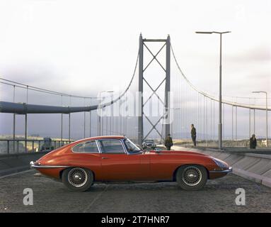 1964 Pressebild des roten Jaguar E-TYPE Series 1 Coupés, TES 1, das auf der Fahrbahn der neu eröffneten Forth Road Bridge in Schottland geparkt ist Stockfoto