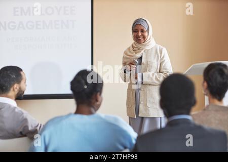 Glückliche junge muslimische Frau in Hijab und Blazer, die vor dem Publikum steht und eine der Jobsuchenden ansieht, die ihre Frage stellt Stockfoto