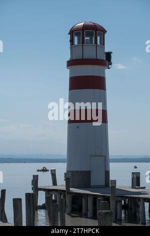 Ein majestätischer Leuchtturm steht hoch auf dem Pier mit seinen roten und weißen Streifen, die sich vom blauen Himmel und dem Meer abheben Stockfoto