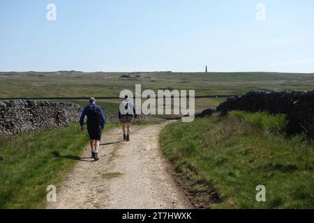 Two Men (Wanderer) Walking on a Track to the Ssmelt Mill Chimney (Flue) in den stillgelegten Grassington Lead Mines im Yorkshire Dales National Park. Stockfoto
