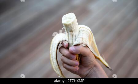 Hand eines Kindes, das eine halb gegessen Banane hält. Nahansicht. Stockfoto