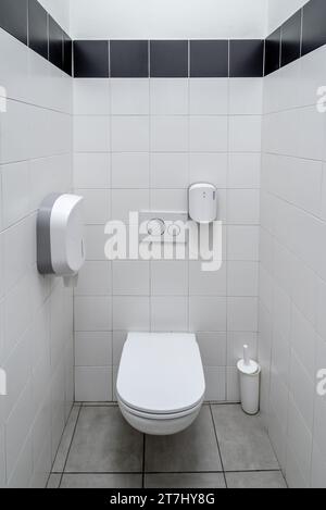 Öffentliche Toilette mit gefliesten Wänden mit weißer Toilettenschüssel mit Papierhalter und Toilettenbürste im Einkaufszentrum Stockfoto