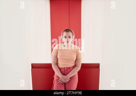 Porträt einer jungen Frau mit Kopfhörern und Blick auf die Kamera im roten Raum Stockfoto