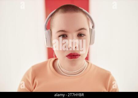 Minimales Nahaufnahme-Porträt einer jungen Frau mit Buzzcut mit Kopfhörern und Blick auf die Kamera im futuristischen Raum Stockfoto