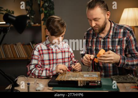 Vater und Sohn reparieren Laptop zu Hause mit Lötkolben und Multimeter zur Diagnose defekter Mainboards Stockfoto