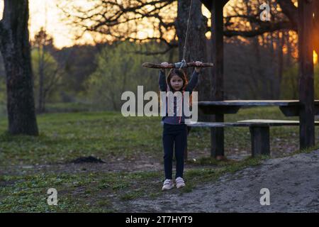 Das charmante kleine Mädchen schwingt auf hausgemachter Schaukel in der Natur, im Park, im Dorf, im Kindercamp. Spiele und Unterhaltung im Freien. Happy ch Stockfoto