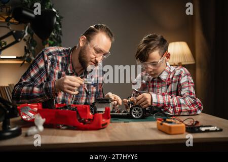 Vater mit Sohn verwendet Lötkolben für die Reparatur von Spielzeugauto zu Hause. Familie und Zweisamkeit. Stockfoto