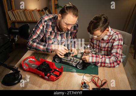 Vater mit Sohn verwendet Lötkolben für die Reparatur von Spielzeugauto zu Hause. Familie und Zweisamkeit. Stockfoto