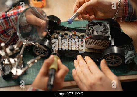 Vater und Sohn verwenden Lötkolben für die Reparatur von Spielzeugautos zu Hause. Das Konzept des Familienhobbys Stockfoto