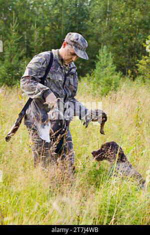 Ein Jäger nimmt während der Jagd ein abgestürztes Auerhühl von einem Hund (deutscher Drahtbarren) Stockfoto