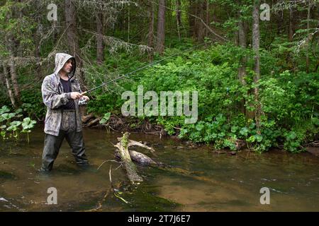 Ein Fischer mit einer Spinnrute in den Händen steht im flachen Wasser an einem kleinen nördlichen Fluss Stockfoto