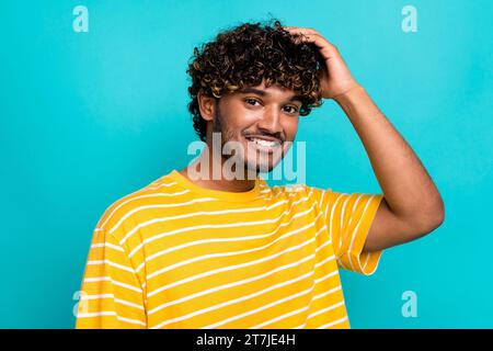 Porträt des attraktiven positiven Mannes Zahny Lächeln Handberührung lockige Frisur lokalisiert auf blaublauem Hintergrund Stockfoto
