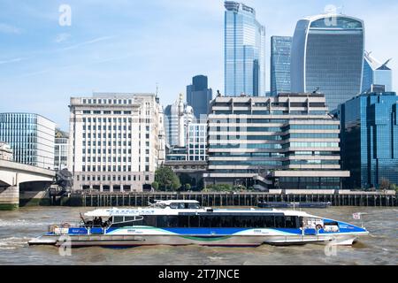 An einem sonnigen Tag mit blauem Himmel fährt ein MBNA-Boot an der Themse Clipper vor den Gebäuden der City of London und den Wolkenkratzern vorbei Stockfoto