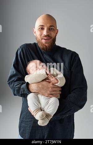 Gutaussehender, fröhlicher Vater hält seinen schlafenden neugeborenen Jungen und lächelt fröhlich in die Kamera, Familie Stockfoto