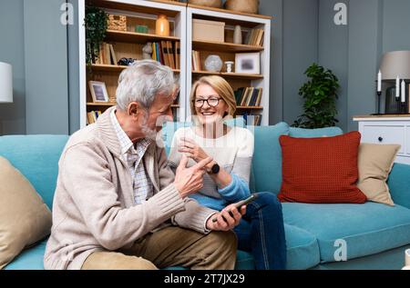 Glückliches älteres Ehepaar, das Smartphone hält und auf den Handy-Bildschirm schaut lachend entspannt sitzen zusammen auf dem Sofa sitzen, lächeln ältere Großeltern Familie Stockfoto