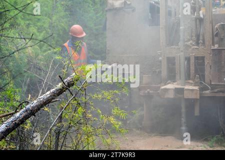 Das Kettenbohrfahrzeug bohrt gut, beim Bohren eines Brunnens ist viel Staub vorhanden. Bohren von Explorationsbrunnen im Wald. Stockfoto