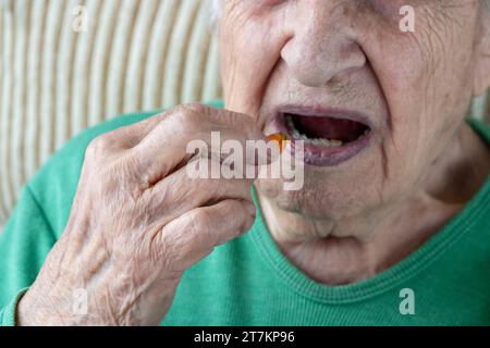 Nahaufnahme Mund und Hand einer Seniorin, die eine Vitaminkapsel einnimmt Stockfoto