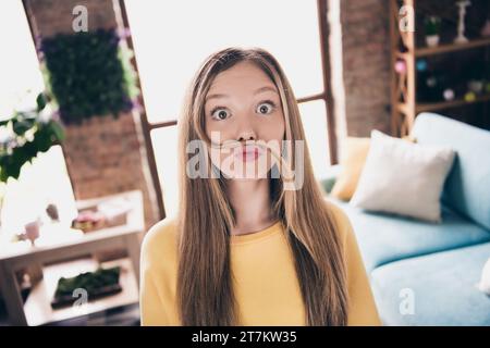 Foto-Porträt von funky Teenager positive Mädchen, die mit ihren blonden Haaren scherzen, Schnurrbart macht, der allein zu Hause bleibt Stockfoto
