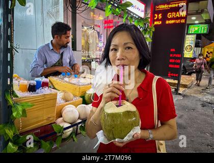 Eine Vietnamesin trinkt eine frische grüne Kokosnuss, die von einem Händler auf den Straßen von Bangkok in Thailand gekauft wurde. Stockfoto