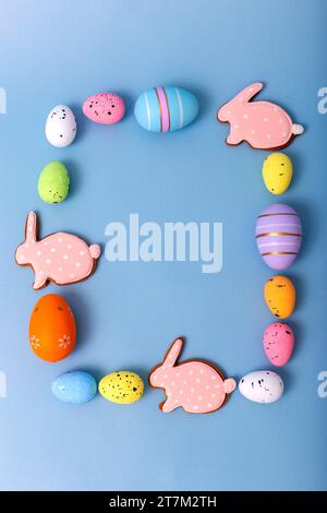 Rechteckiger Rahmen von mehrfarbigen Ostereiern und Lebkuchen in Form von rosa Kaninchen Stockfoto