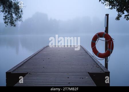 Hölzerner Pier im blauen Morgennebel, mit einem Rettungsring, der an einer Stange hängt Stockfoto