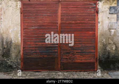 Rote Doppeltüren aus Holz und abgenutzte Zementwand eines antiken Gebäudes. Stockfoto