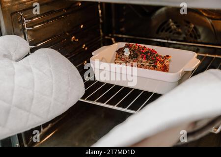 Hände in Topflappen nehmen Roastbeef aus dem Ofen. Festliches Weihnachtsessen Stockfoto