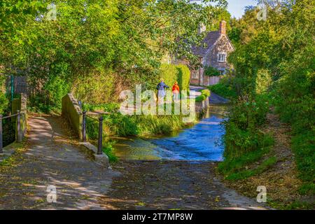 Der Bide Brook ford und die Fußgängerbrücke auf dem Nethercote Hill in Lacock Village, Wiltshire, England, Großbritannien Stockfoto