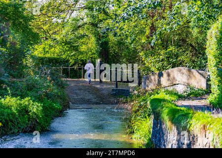 Der Bide Brook ford und die Fußgängerbrücke auf dem Nethercote Hill in Lacock Village, Wiltshire, England, Großbritannien Stockfoto