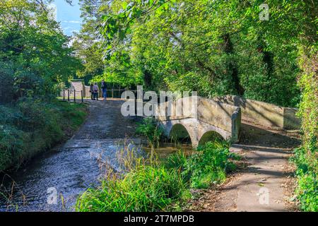 Der Bide Brook ford und die Fußgängerbrücke auf dem Nethercote Hill in Lacock Village, Wiltshire, England, Großbritannien Stockfoto