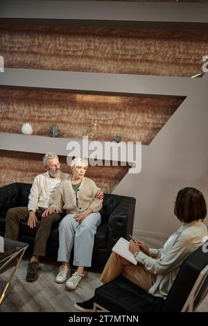 Ein bärtiger Mann umarmt eine besorgte Frau mittleren Alters während einer Therapiesitzung mit dem Familienberater Stockfoto