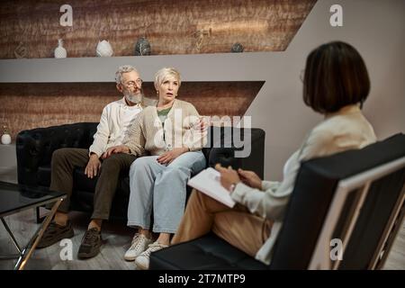 Ein bärtiger Mann umarmt eine besorgte Frau mittleren Alters während einer Therapiesitzung mit dem Familienberater Stockfoto