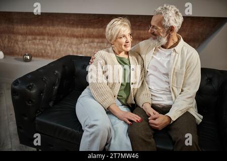 Glückliches Paar mittleren Alters, das sich während der Familientherapie umarmt und auf einer Ledercouch sitzt Stockfoto