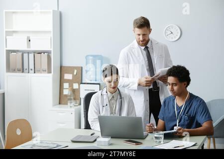 Multiethnische Gruppe von Ärzten mit Laptop und Zusammenarbeit am Schreibtisch in der Klinik, Kopierraum Stockfoto