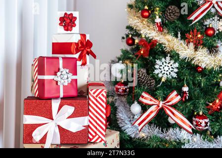 Ordentlich verpackte Geschenkboxen unter dem modernen Weihnachtsbaum in einem Haus, ergänzt durch Weihnachtsschmuck, eine festliche Neujahrsdekoration. Stockfoto