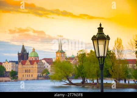 Verschwommener Blick auf die Insel Strelecky auf der Moldau und die Altstadt von Prag, Tschechien, bei Sonnenuntergang. Selektiver Fokus auf das Straßenlicht Stockfoto