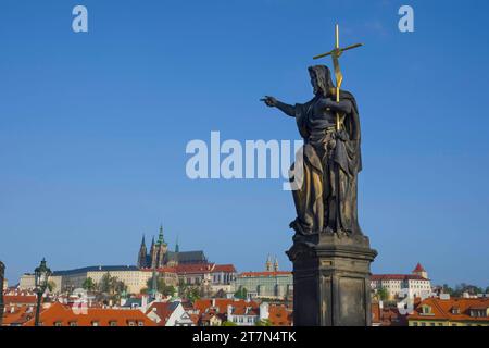 Statue von St. Johannes der Täufer auf der Karlsbrücke, mit Hradcany Castle und St. Vitus Kathedrale im Hintergrund, in Prag, Tschechien, an sonnigem Tag Stockfoto