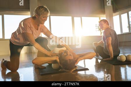 Yogalehrer hilft einem Schüler beim Dehnen und Massagen in einem sonnendurchfluteten Raum Stockfoto