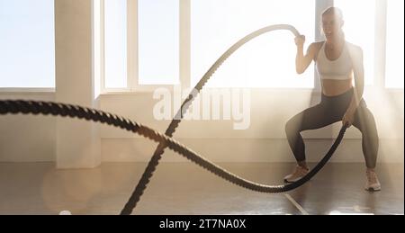 Junge athletische Frau mit perfektem Körper, die Crossfit-Übungen mit einem Seil im Fitnessstudio macht. Stockfoto